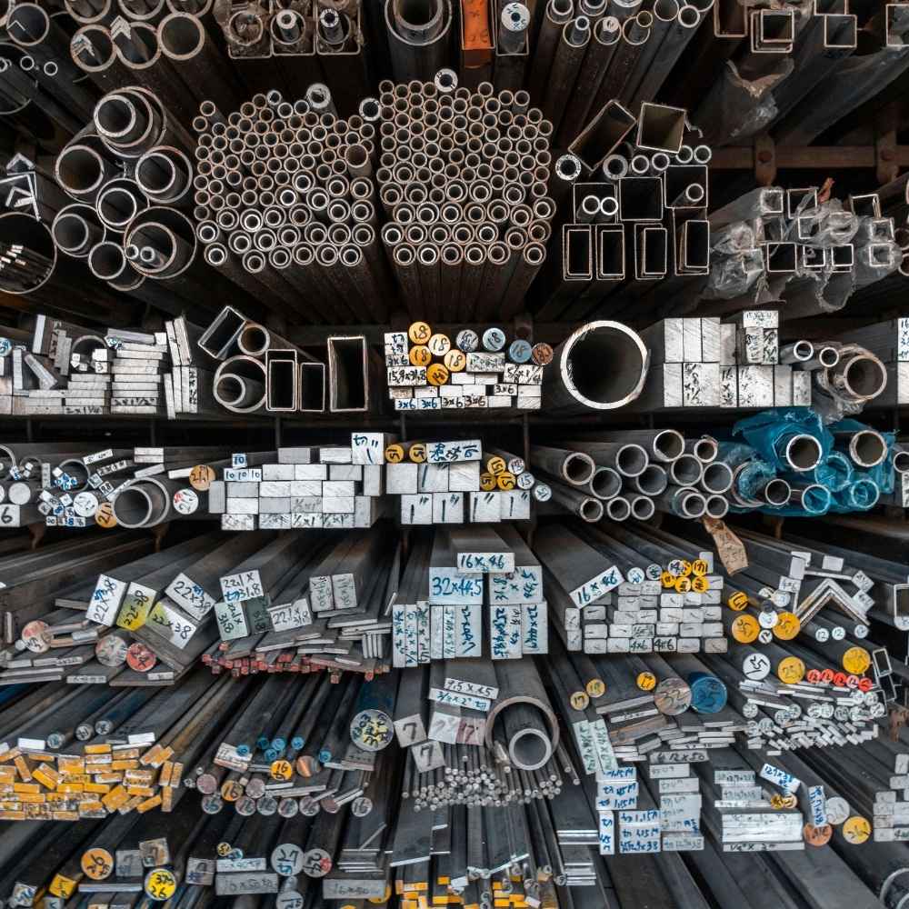 Warehouse inventory from an aluminium supplier showing stacked aluminum profiles and tubes for pergola shed frames.