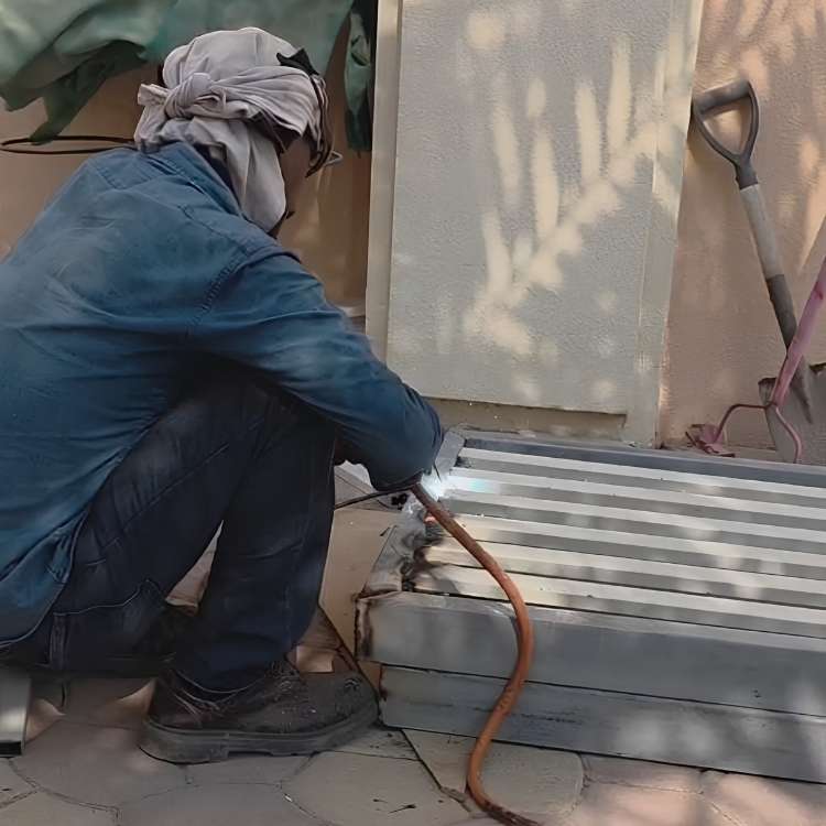 Worker welding metal frames on-site during custom steel fabrication for a outdoor pergola structure.